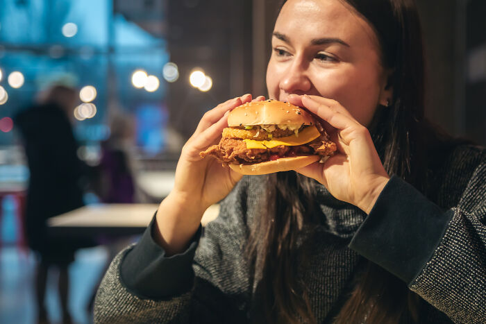 Woman holding a burger and smiling inside a restaurant illustrating customers ridiculous complaints and employee reactions.