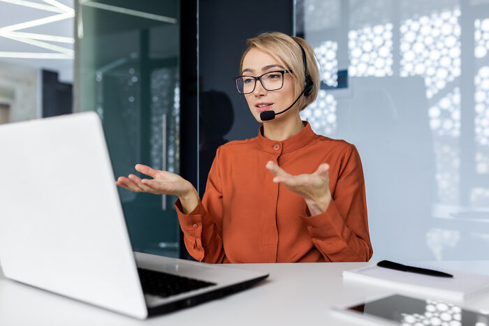 Customer service employee with headset reacting to ridiculous complaints while working at a laptop in a modern office.
