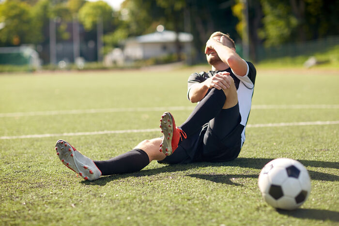 Soccer player sitting on field holding knee in pain, illustrating a very quick shortcut to personal hell concept.