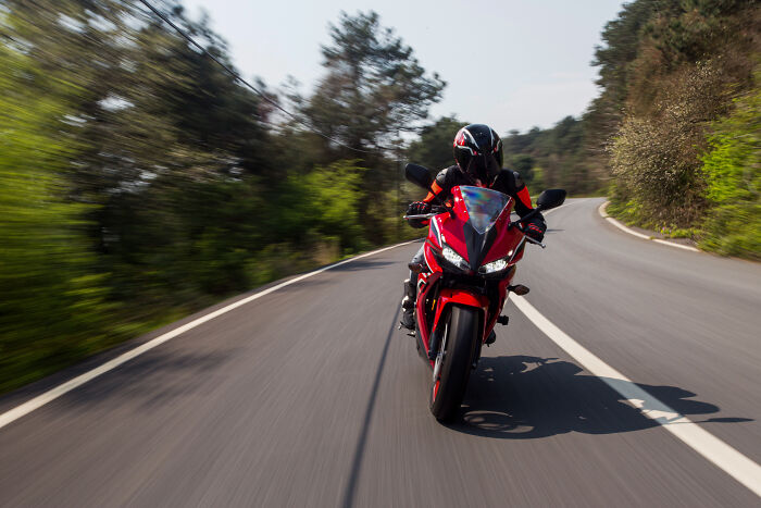 Motorcyclist riding a red sportbike on a winding road surrounded by trees, illustrating a shortcut to personal hell.