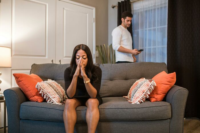Woman looking distressed on a couch with a worried man standing in the background, illustrating personal hell and ruined lives.