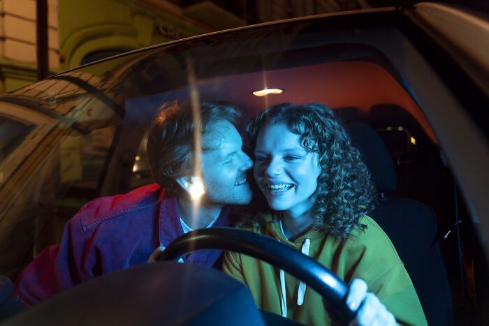 Couple in car at night, smiling and close together, illustrating a moment of personal connection and emotional experience.