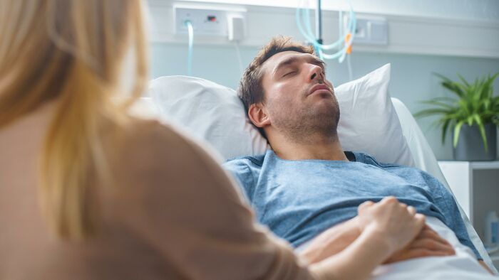 Man lying unconscious in hospital bed with a woman holding his hand, illustrating sobering stories of ruined lives.