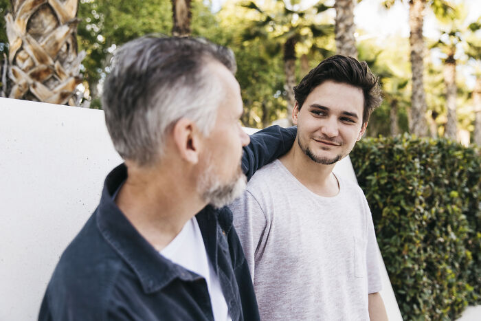 A dad and his teenage son smiling outdoors, showing wholesome support and care between father and child.