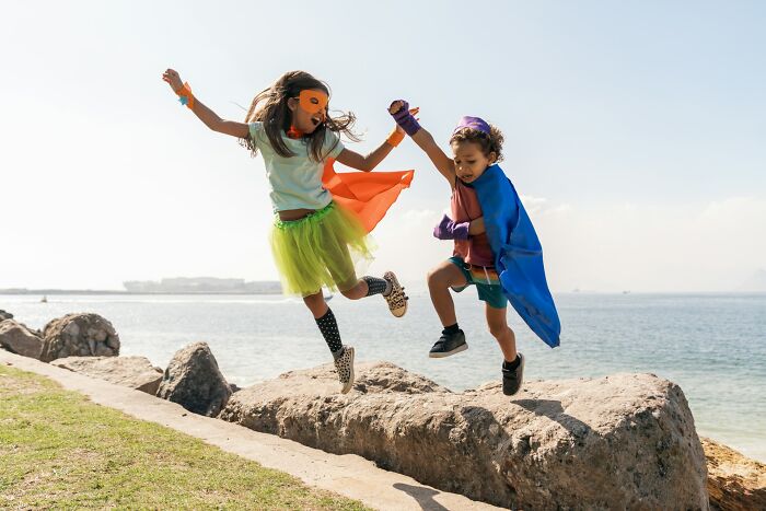 Two children dressed as superheroes jumping on rocks by the ocean, symbolizing forgiveness after cheating spouse struggles.