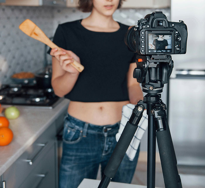 Jovem filmando a si mesma na cozinha com a câmera no tripé, relacionada à história viral de prisão de uma mulher na Flórida. Jovem filmando a si mesma na cozinha com a câmera no tripé, relacionada à história viral de prisão de uma mulher na Flórida.