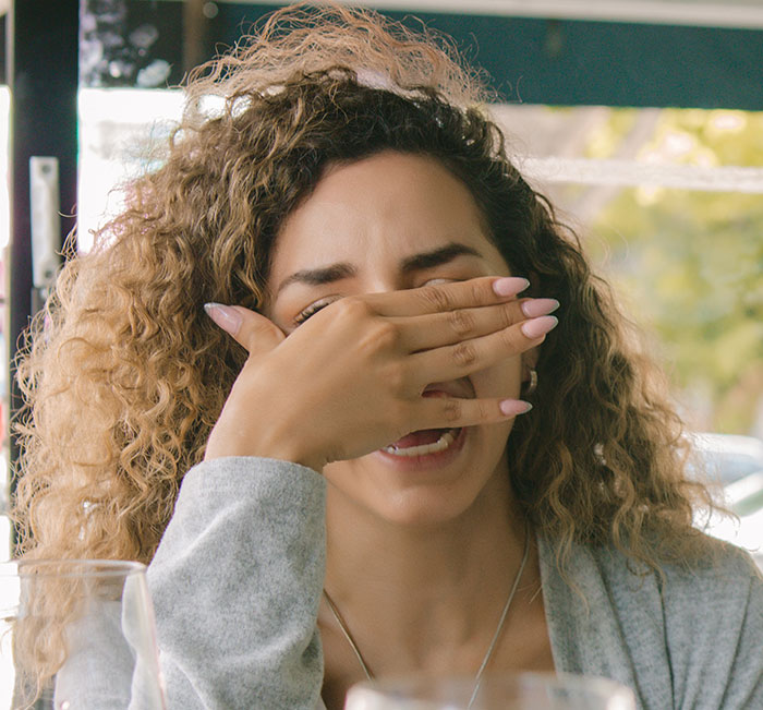 Woman with curly hair covering her face in embarrassment during a first date, showing first dates so horrible symbolism.