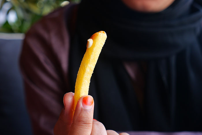 Person holding a single fry with a bite and ketchup, illustrating first dates so horrible they build character trauma.