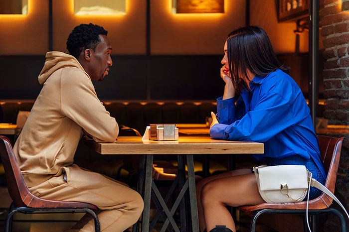 A tense first date between a man and woman in a dimly lit restaurant, showing uncomfortable body language.