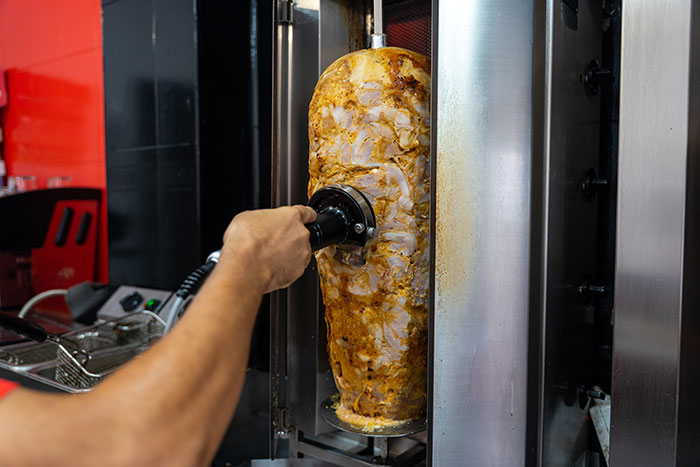 Hand slicing seasoned meat on a vertical rotisserie, representing a first date with character-building trauma in a food setting.