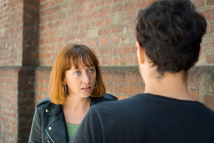 A woman looking shocked and confused during a tense conversation on a first date outside by a brick wall.