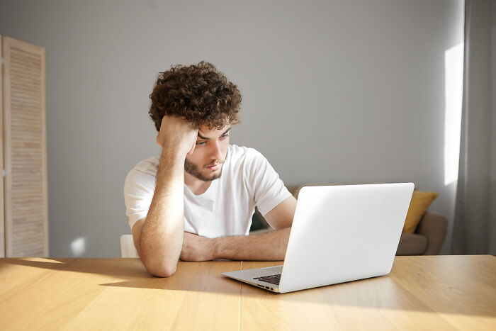 Young man with curly hair looking thoughtfully at a laptop, depicting themes of ex incels and personal change.
