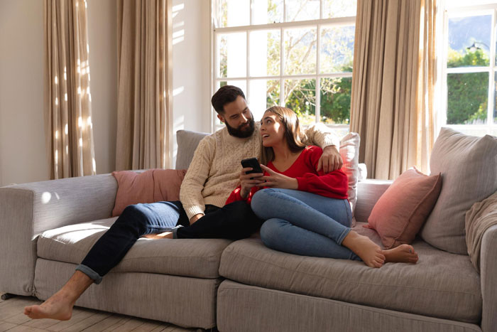 Couple sitting on a couch, the woman in red holding a phone, relating to SIL calls pregnant woman a beached whale topic.