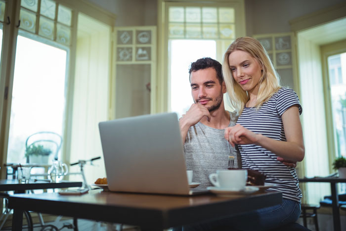 Couple sitting in a cafe looking at a laptop screen, illustrating SIL calls pregnant woman a beached whale story.