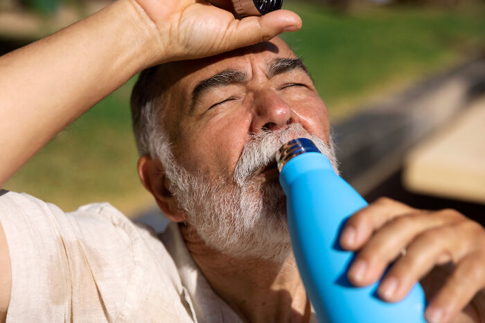 Older man with gray beard outdoors drinking water from a blue bottle, reflecting on wild things funeral directors saw.