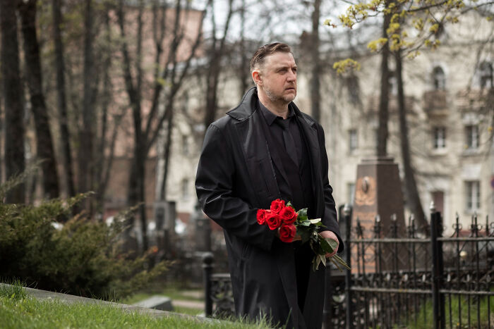 Man in black coat holding red roses in a cemetery, reflecting on wild things funeral directors still remember.