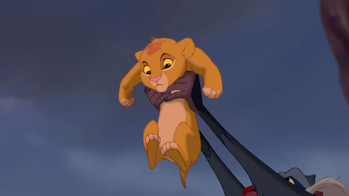 Animated scene of a young lion cub held up by a dark-furred animal, capturing a memorable moment from the film.