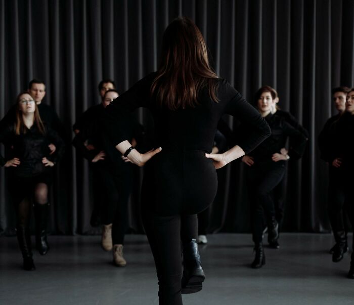 Group of people dressed in black practicing coordinated moves in front of dark curtains, evoking funeral director scenes