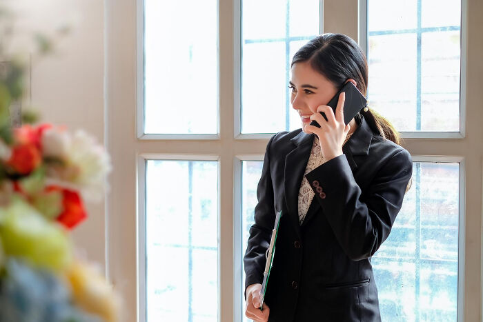 Funeral director in a black suit talking on phone near window, recalling wild things they still remember.