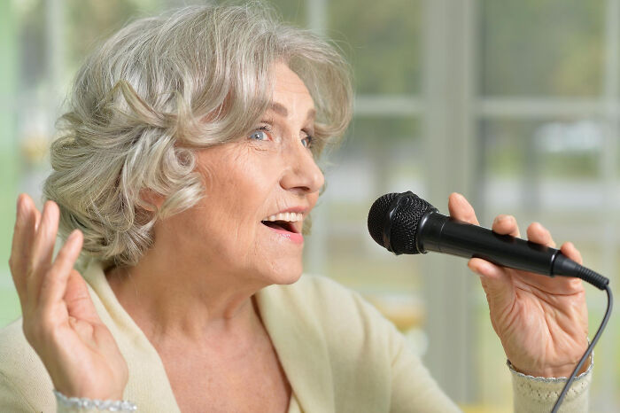 Elderly woman singing into microphone captured in a candid moment, relating to funeral directors' wild memorable experiences.