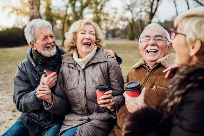 A group of elderly friends laughing and holding coffee cups outdoors, capturing memorable moments funeral directors recall.
