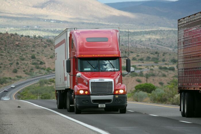 Red semi truck driving on a highway through a desert landscape, representing wild things funeral directors saw.