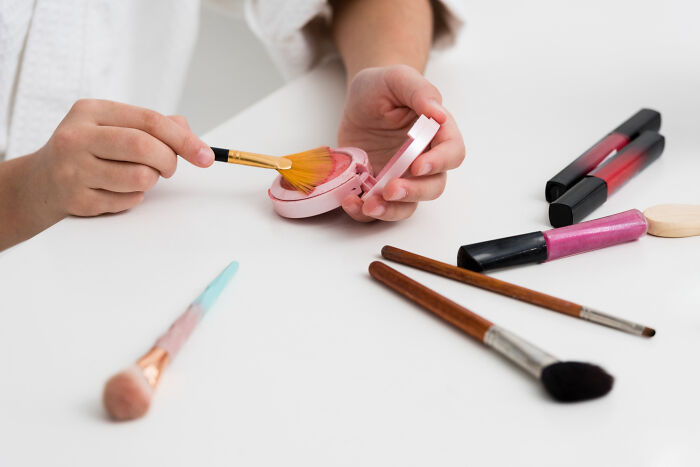 Person holding a makeup brush applying blush with cosmetic tools on a white table, related to funeral directors' wild things seen.