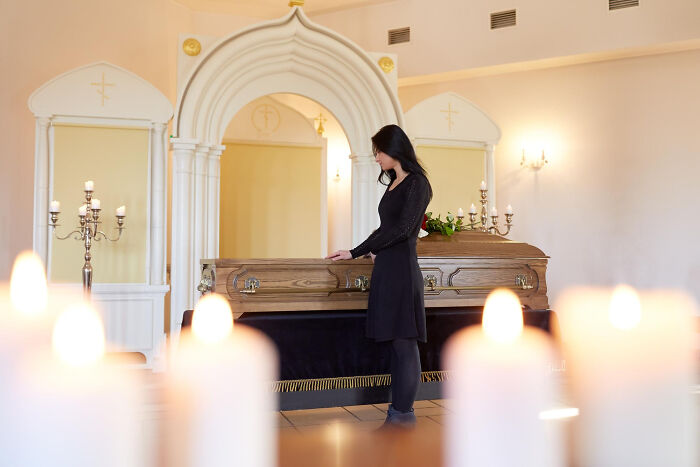 Woman in black standing beside a coffin in a funeral home, evoking wild things funeral directors still remember.