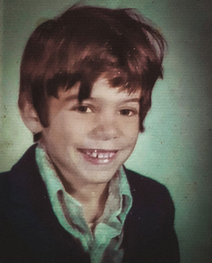Childhood photo of a smiling boy with a messy hair disaster and missing front teeth, wearing a collared shirt and jacket.