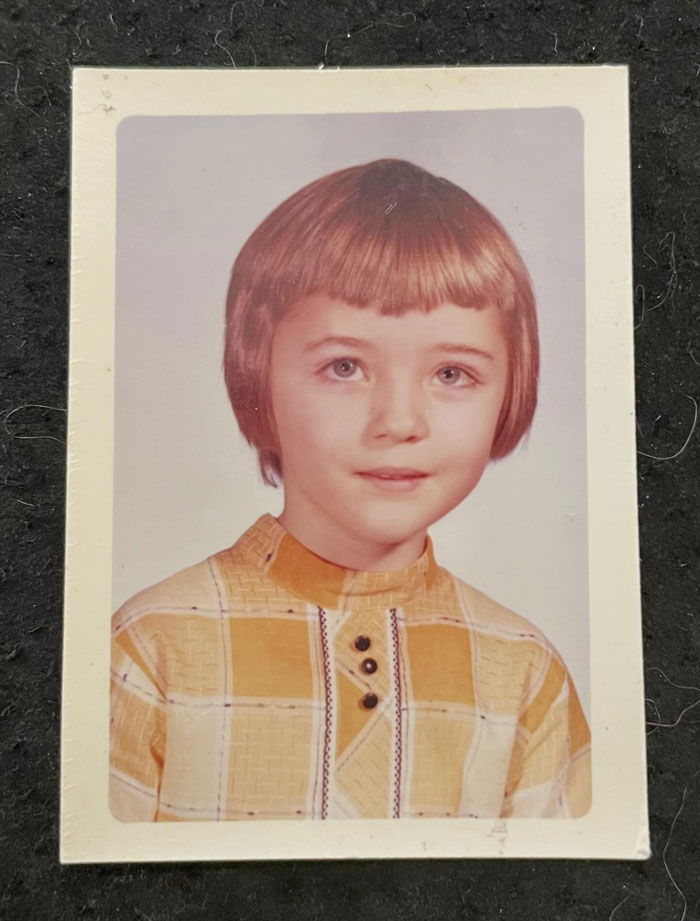 Childhood photo of a young child showing a hair disaster with an uneven, choppy haircut and a plaid yellow shirt.