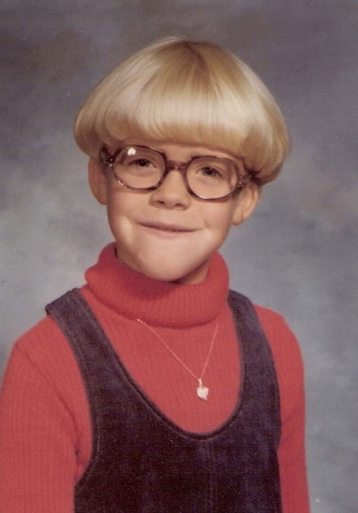Childhood photo showing a young child with a classic hair disaster bowl cut wearing glasses and a turtleneck sweater.