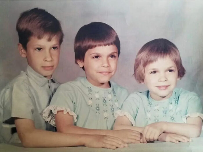 Three children with childhood hair disasters posing for a vintage photo in matching outfits and unique hairstyles.