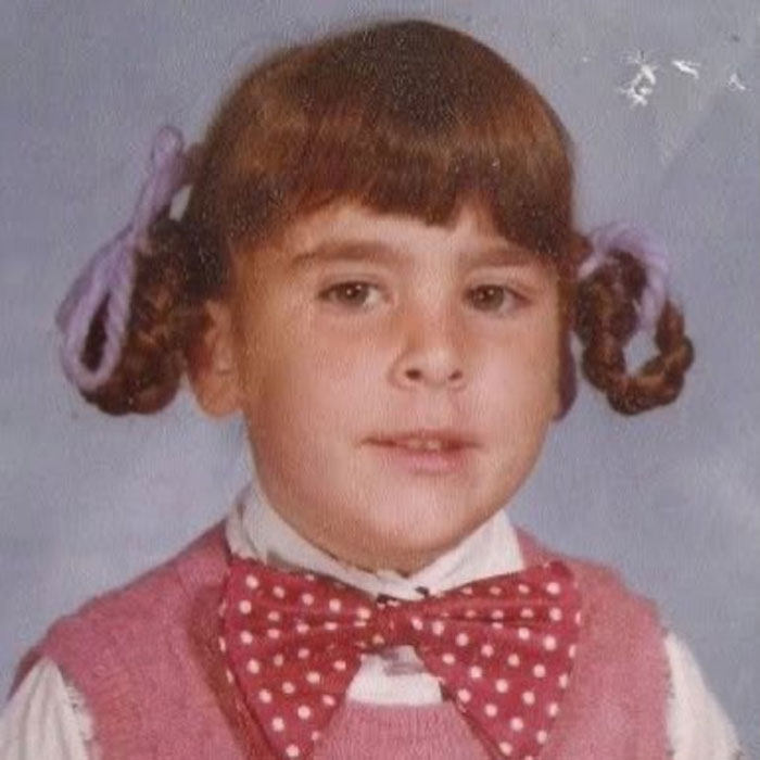 Childhood photo of a young girl with braided pigtails tied with ribbons, showcasing a classic hair disaster style.