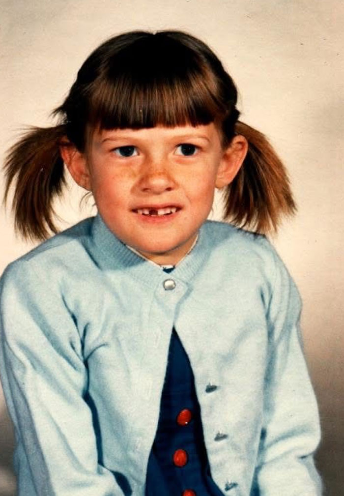 Childhood photo of a girl with a hair disaster hairstyle featuring uneven bangs and messy pigtails, wearing a light blue sweater.