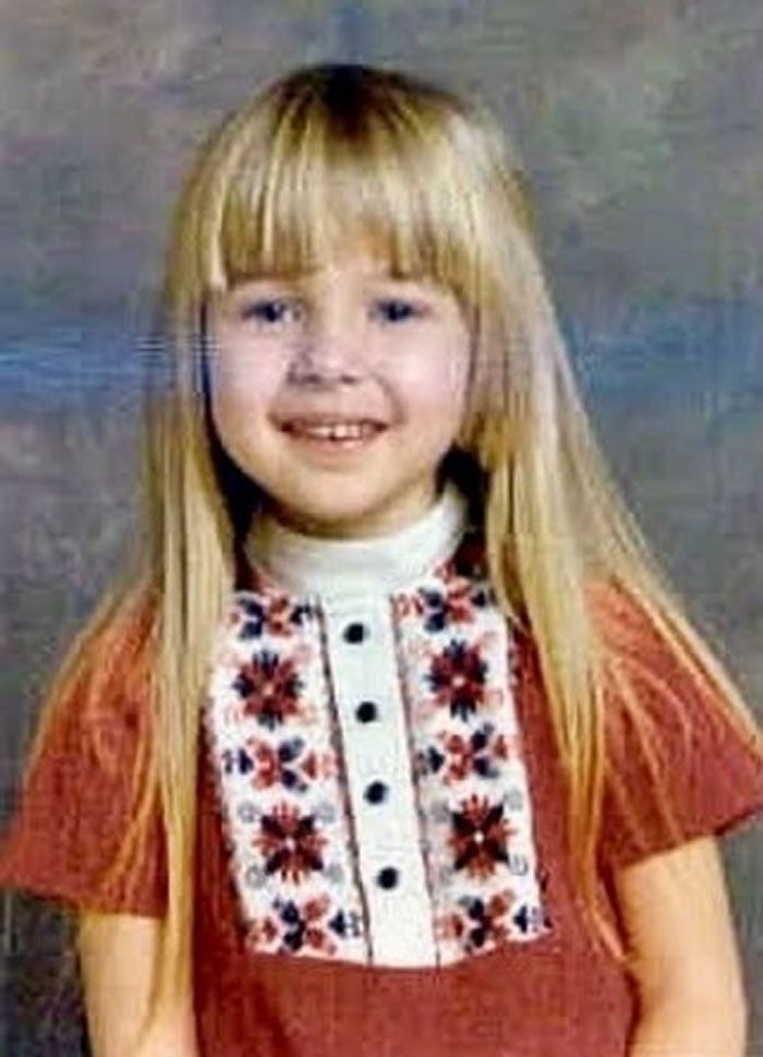 Child smiling girl with long blonde hair and bangs, showcasing a childhood hair disaster in a vintage school photo.