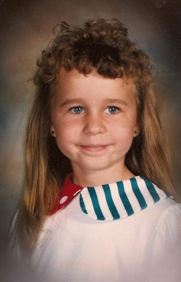 Young girl with a childhood hair disaster hairstyle featuring uneven curls and long straight hair, smiling in a portrait.