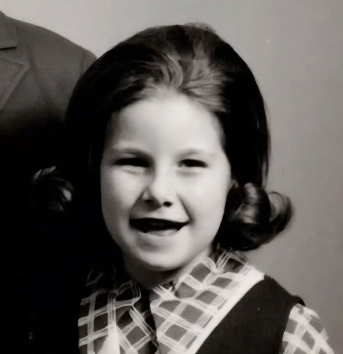 Childhood photo of a young girl smiling with a vintage hairstyle showing a classic hair disaster from the past.