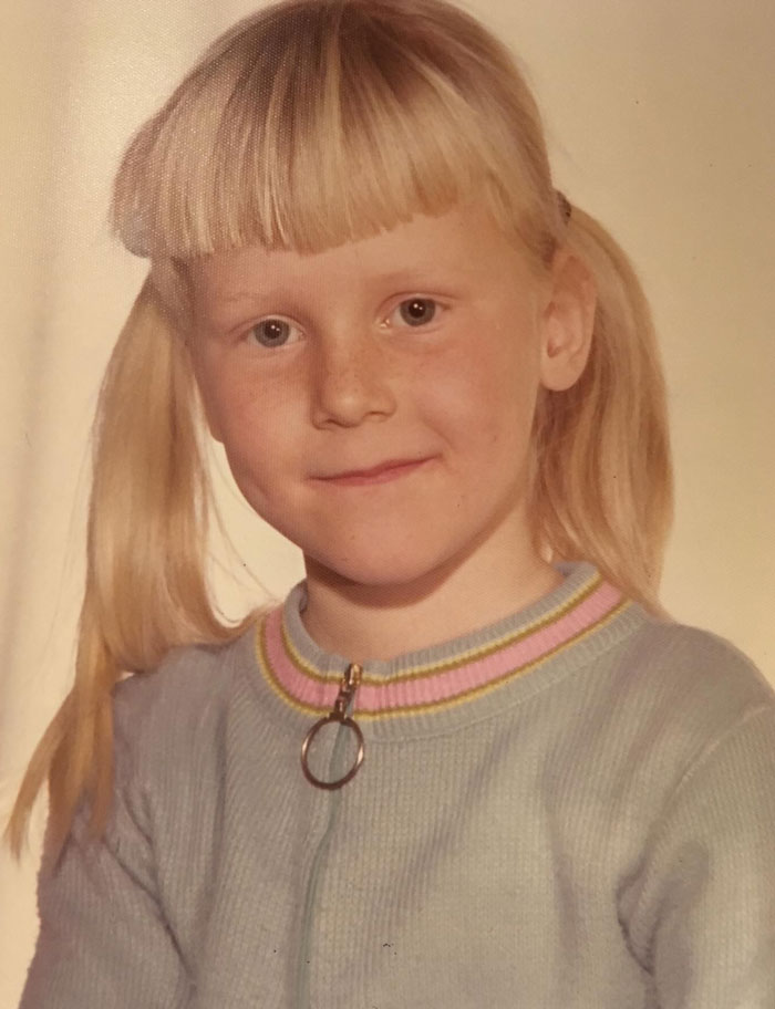 Child with hair disaster sporting uneven blunt bangs and pigtails wearing a blue sweater with a colorful collar.