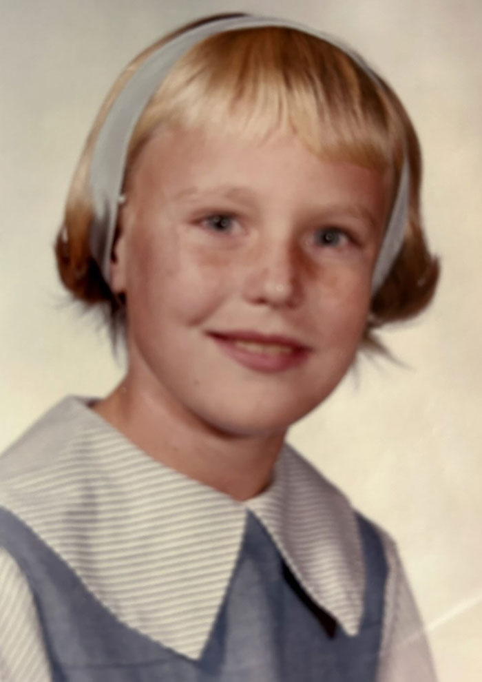 Childhood photo of a girl with a vintage hair disaster style wearing a headband and a collared dress.