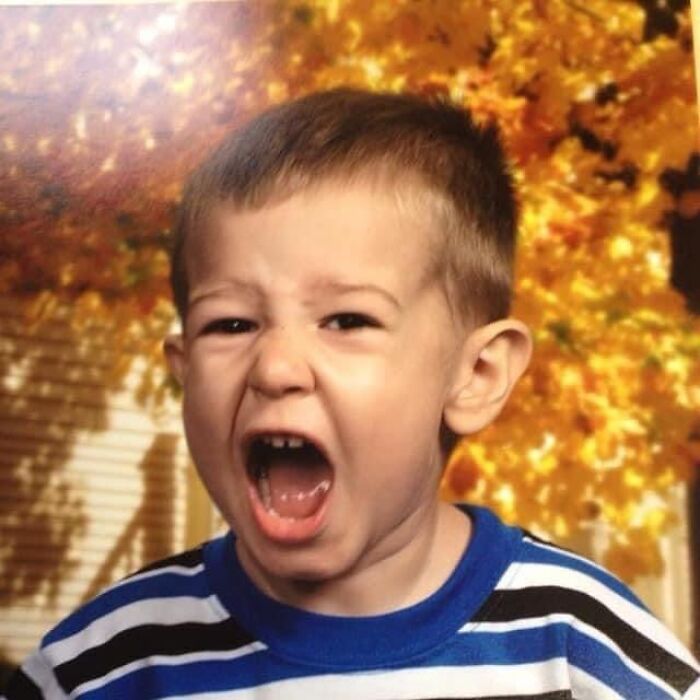 Young boy making a funny face during a school picture day fail with autumn leaves in the background.