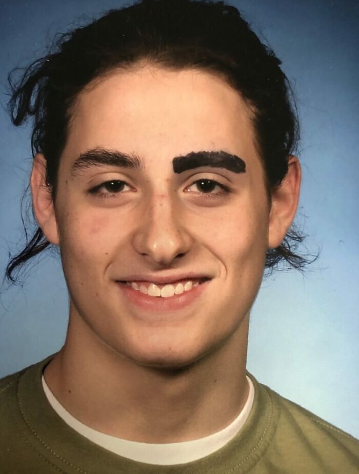 Teen with uneven, thick black eyebrow drawing smiling in a school picture day fail with blue background and green shirt.