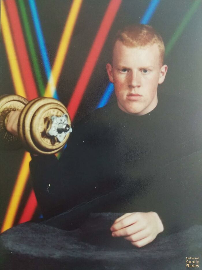 Teen boy posing with dumbbell during funny school picture day fails against colorful striped backdrop.