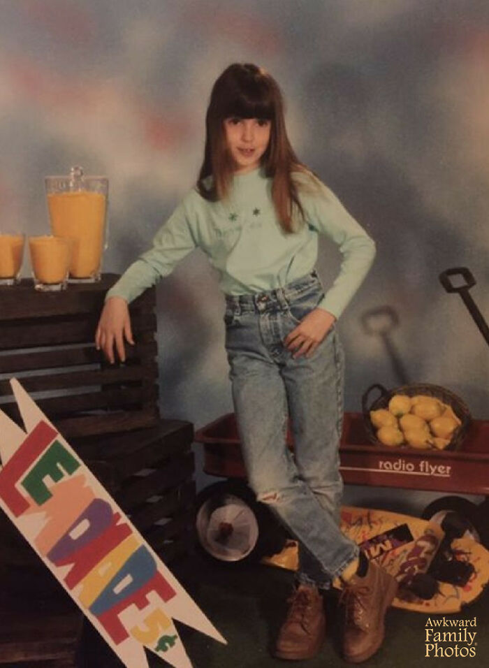 Girl posing awkwardly in a funny school picture day fail with a lemonade stand and a red wagon full of lemons.