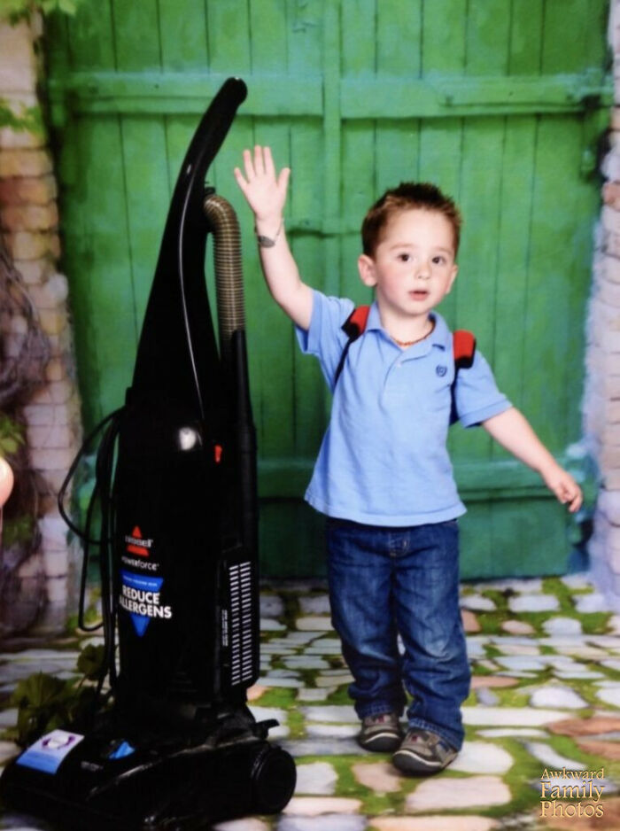 Young boy with backpack waving next to a vacuum cleaner in a funny school picture day fail setting.