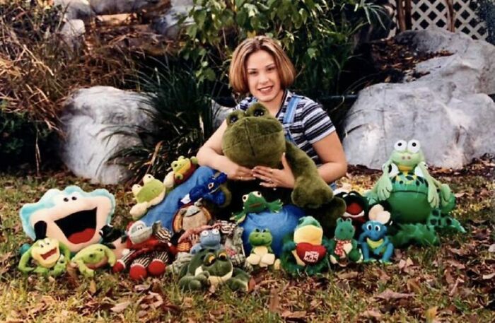 A young girl surrounded by various frog plush toys in an outdoor setting, a funny school picture day fail.