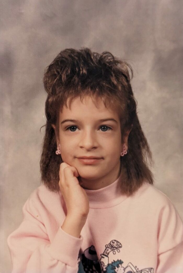 Young student with a unique hairstyle and pink sweatshirt posing for a funny school picture day fail portrait.