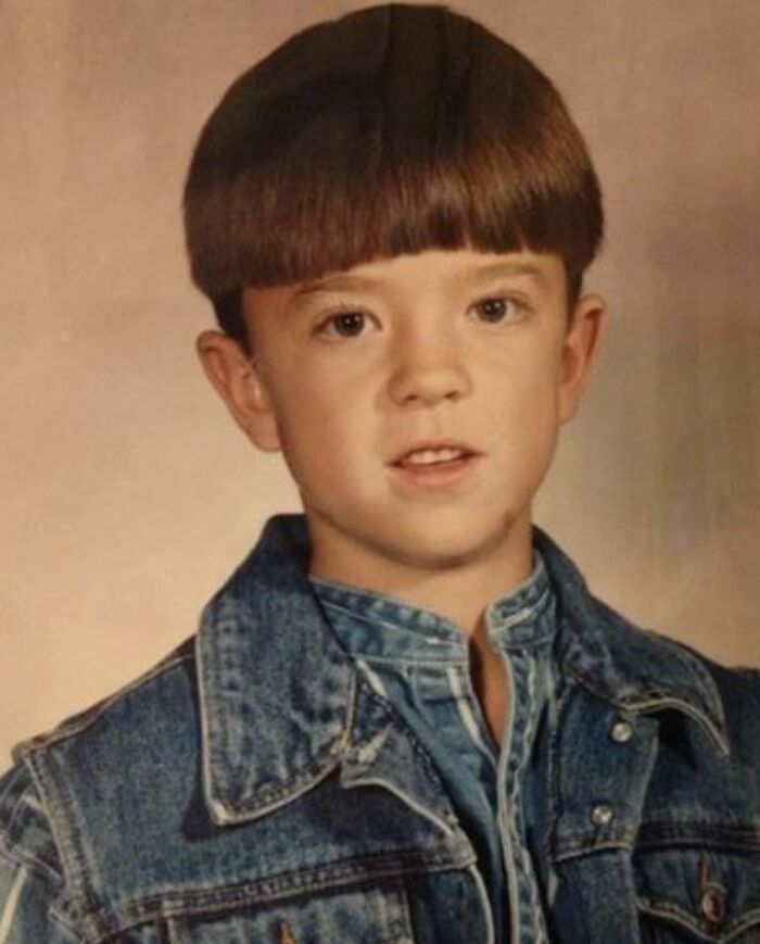 Young boy in a denim jacket with a bowl haircut posing for a funny school picture day photo fail.