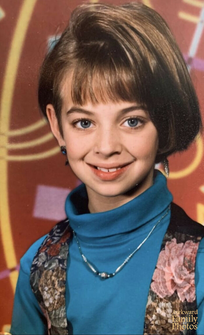 Young girl smiling awkwardly with a colorful patterned vest and blue turtleneck in a funny school picture day fail pose.