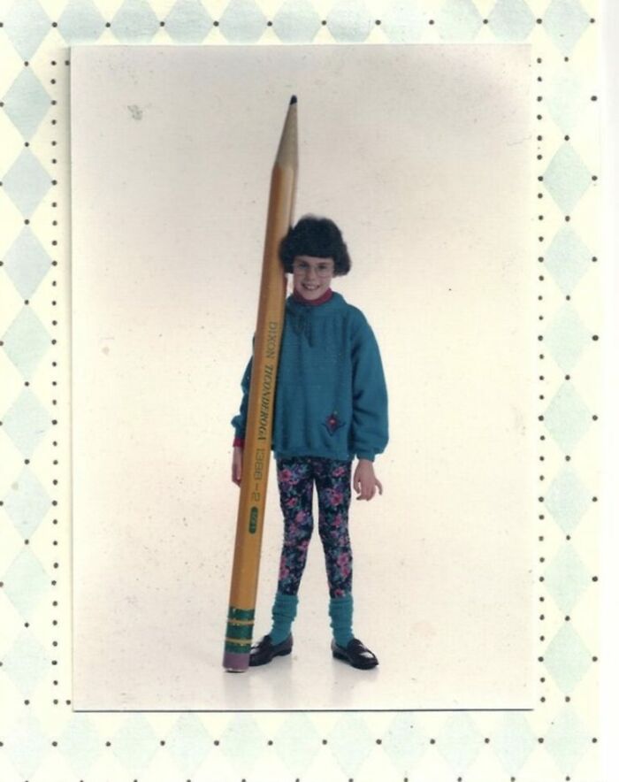 Young girl in colorful outfit posing with an oversized pencil in a funny school picture day fail photo.