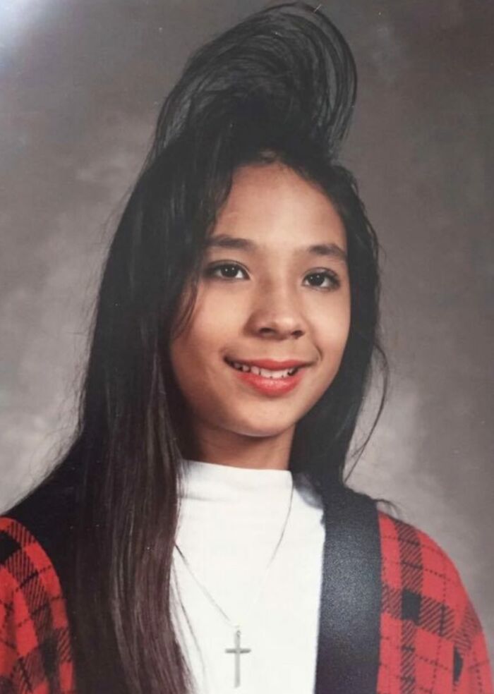 School picture day fail with girl’s hair styled awkwardly high, smiling in a red plaid jacket and white turtleneck.